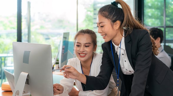 woman pointing to computer showing second woman something on screen